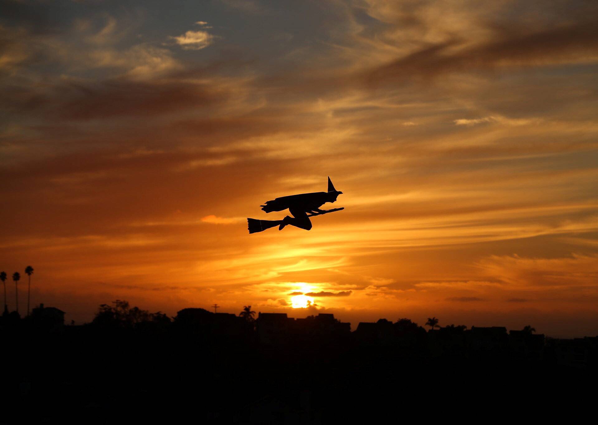 A remote-controlled plane in the form of a witch flies over a neighborhood as the sun sets during Halloween in Encinitas