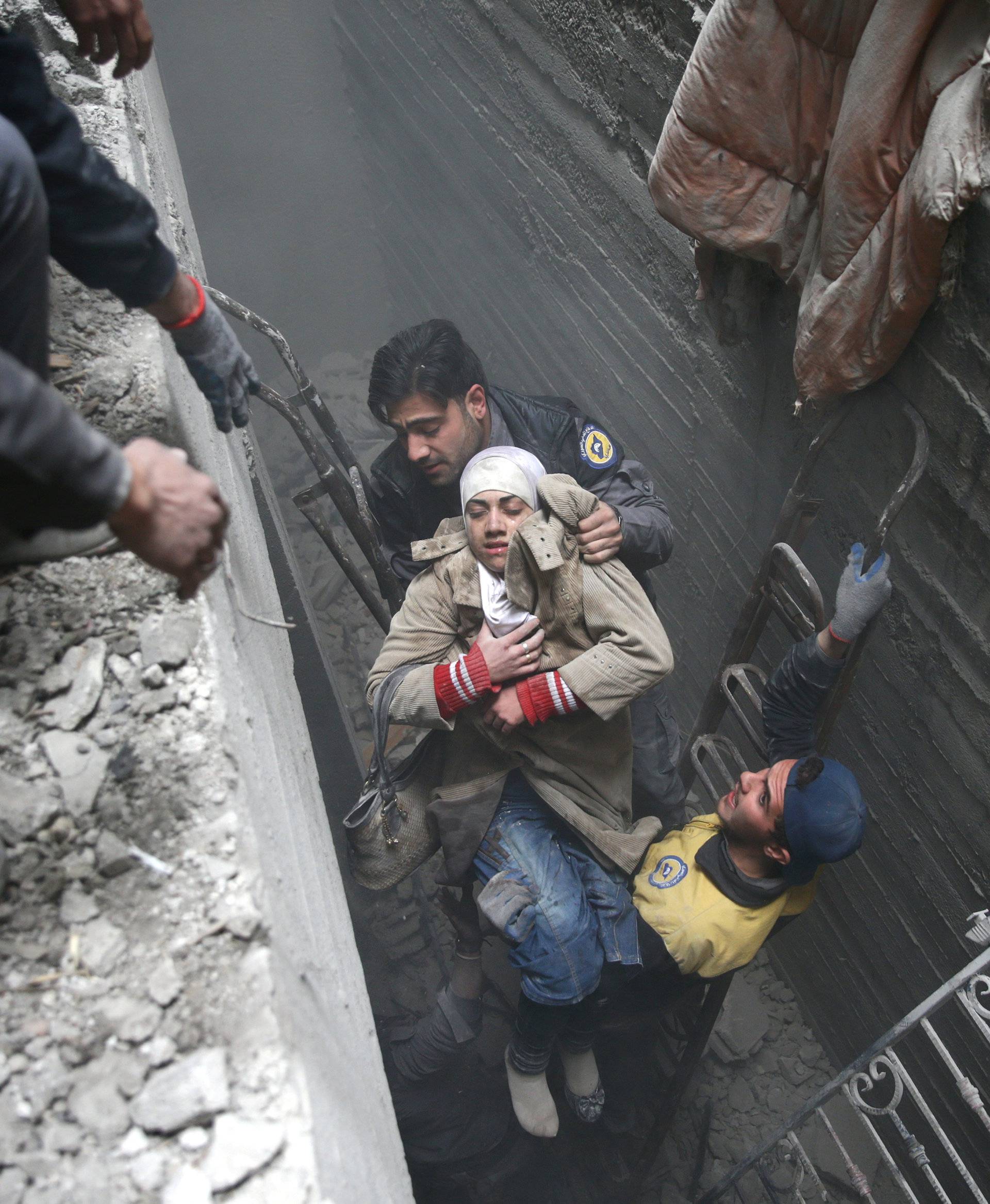 Syria Civil Defence members help an unconscious woman from a shelter in the besieged town of Douma