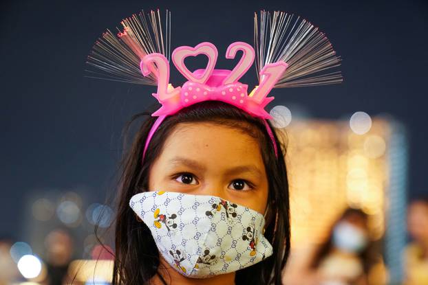 A girl wearing a mask and "2021" head band looks on in Bangkok