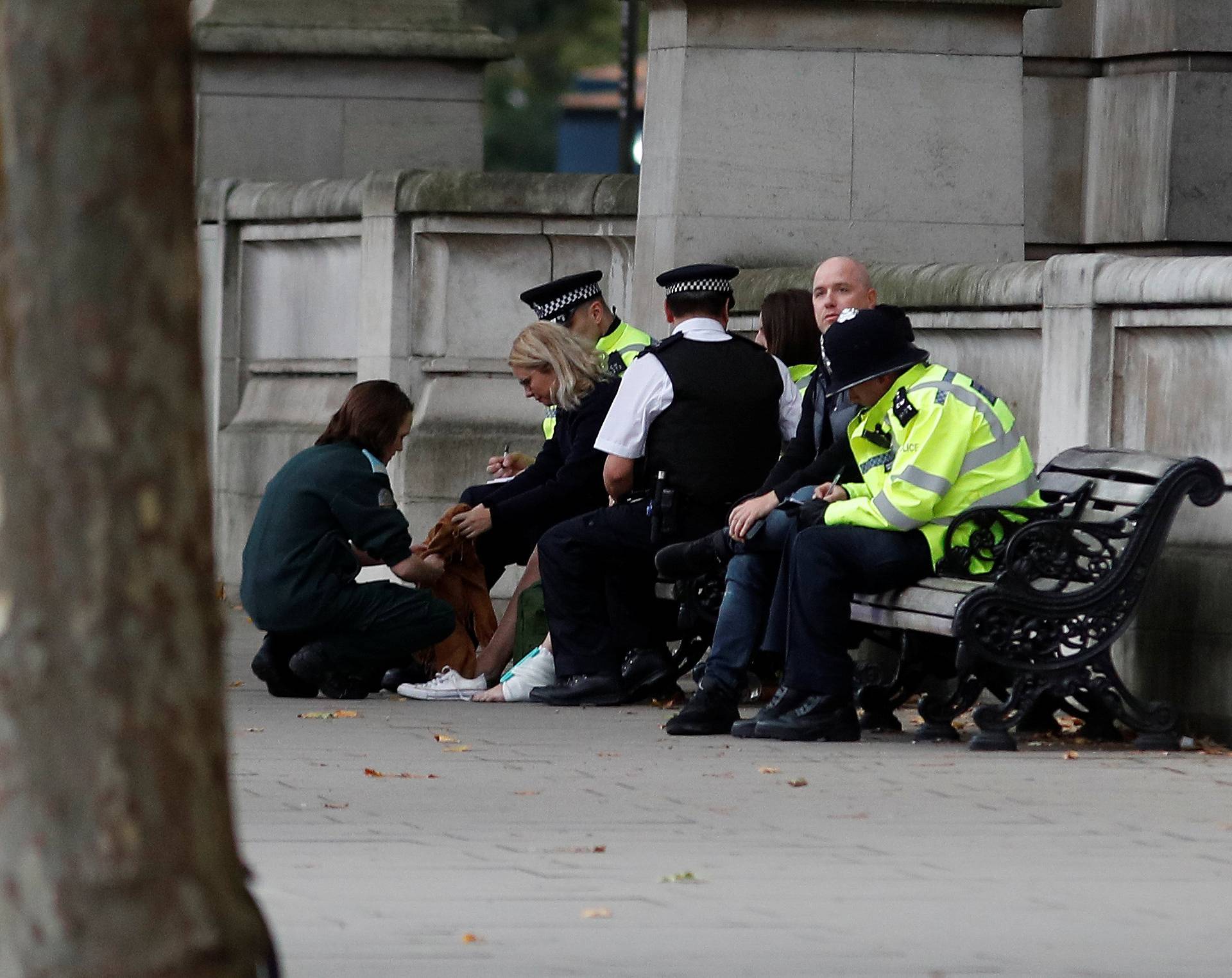 Police officers sit next to a person with a bandaged ankle near the Natural History Museum, after a car mounted the pavement, in London