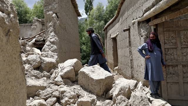 Afghan men stand on the debris of their house that was damaged by an earthquake in Gayan