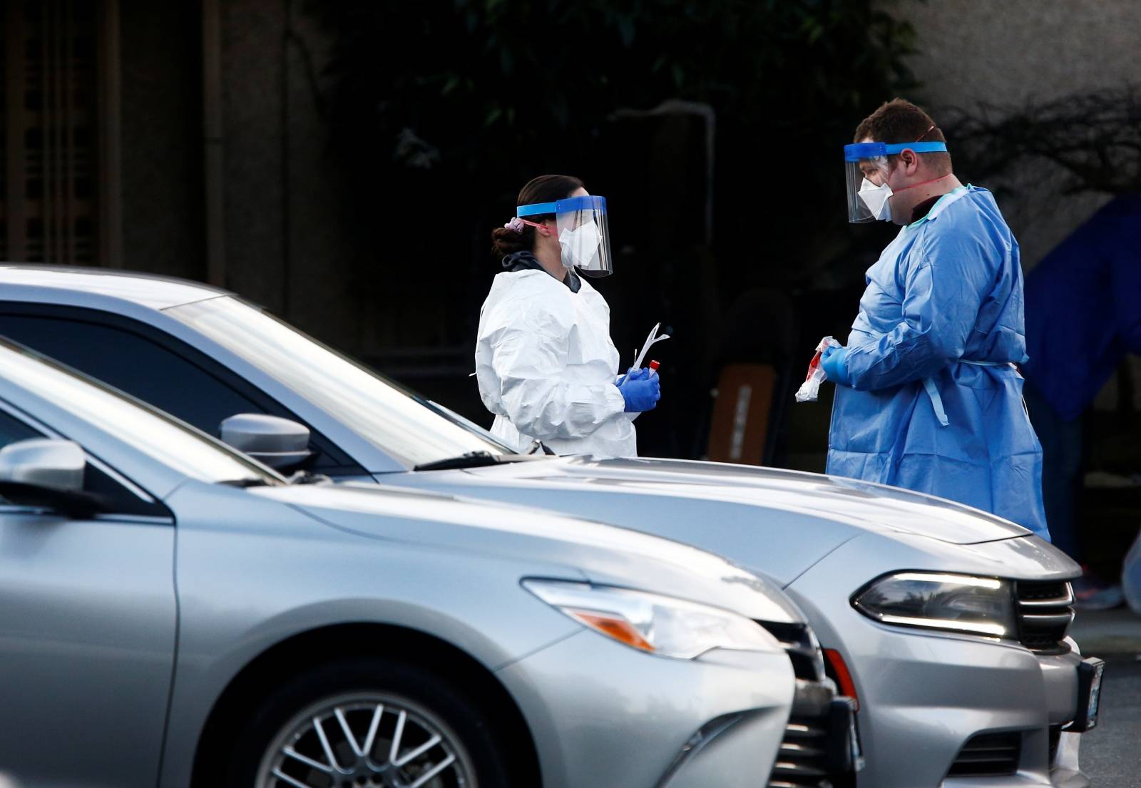 Nurses in protective gear talk before administering a drive-through nasal swab test at Life Care Center of Kirkland