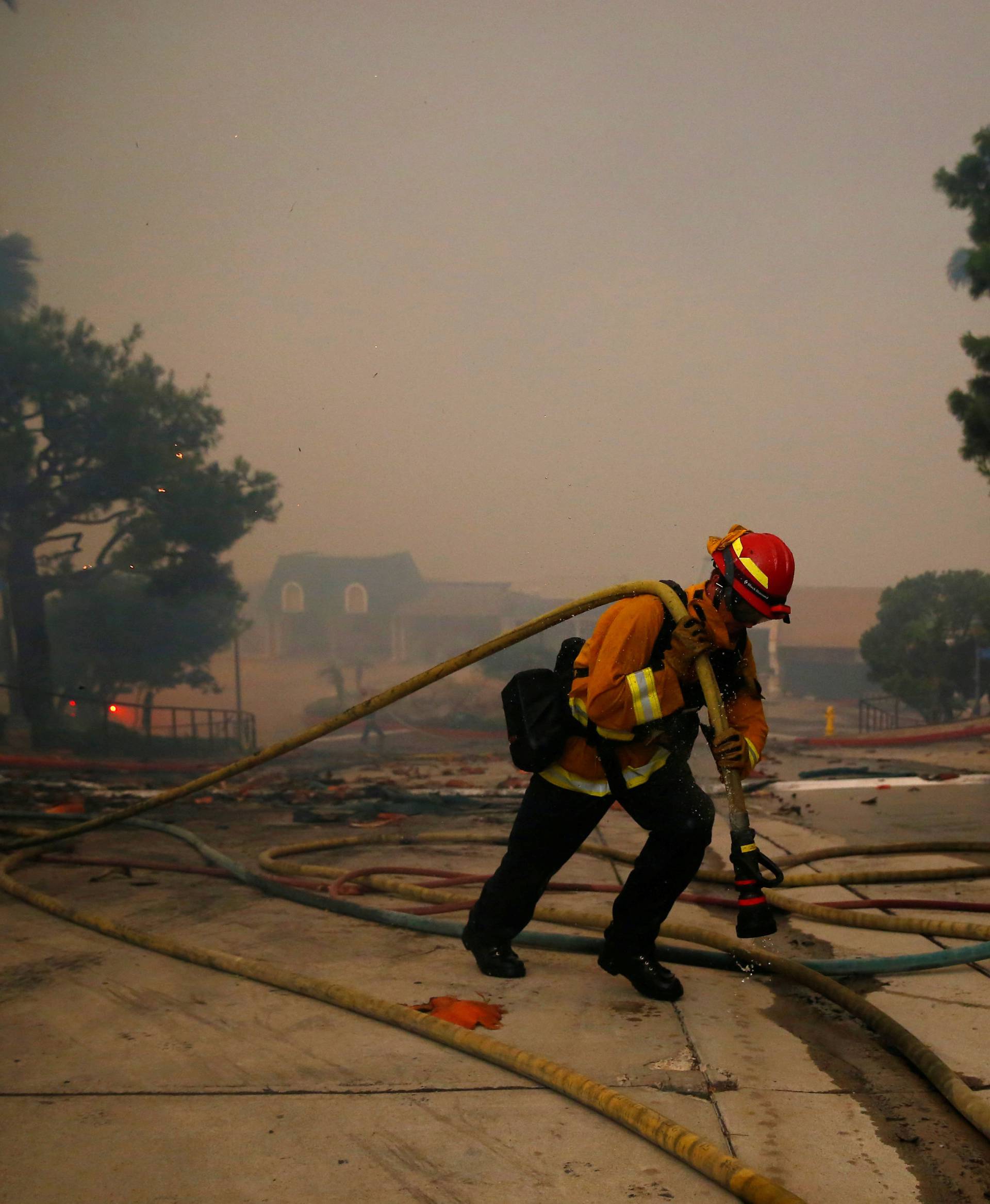 A firefighter carries a hose through an apartment complex as the Woolsey Fire burns in Malibu
