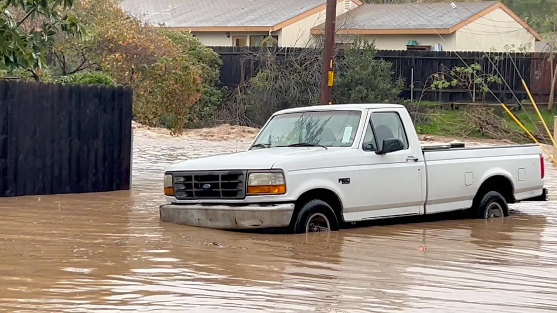 A vehicle lies partially submerged on a flooded street in Santa Barbara