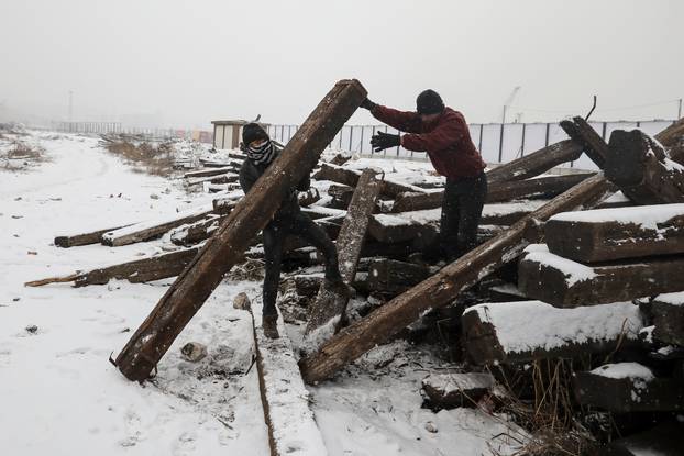 Migrants take away a railway sleeper during a snowfall outside a derelict customs warehouse in Belgrade