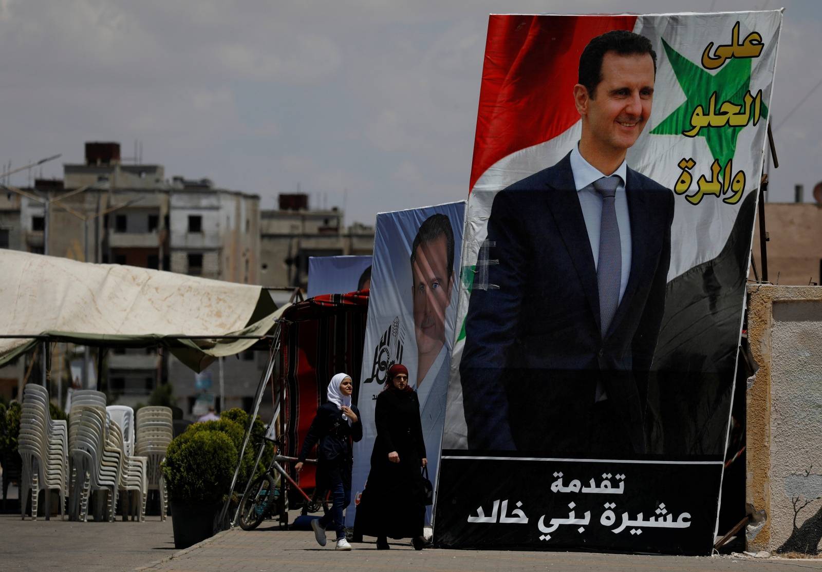 People walk past posters depciting Syria's President Bashar al-Assad, in the district of al-Waer