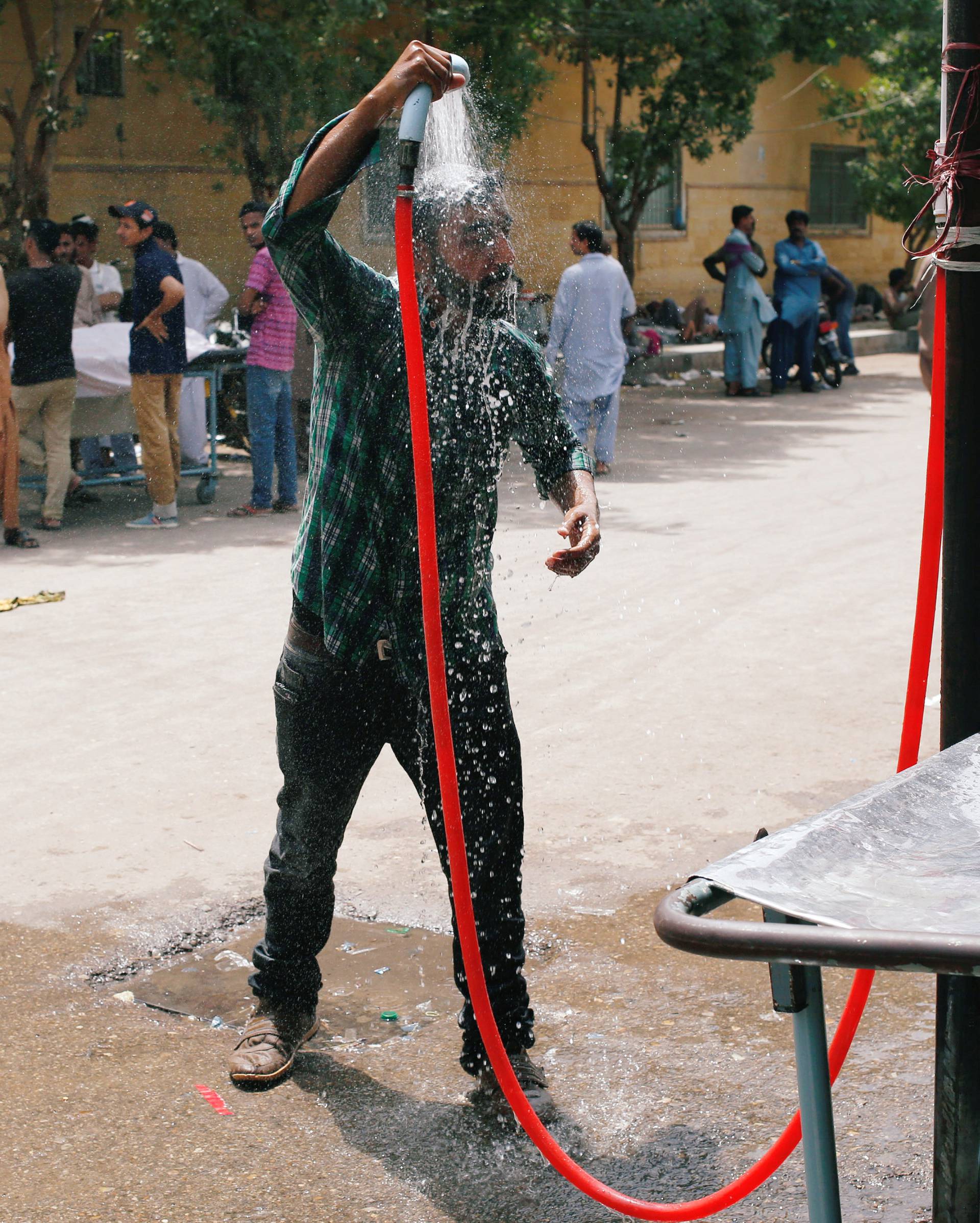 A man cools off with a shower, setup at the premises of the Dr. Ruth K. M. Pfau Civil Hospital, during a heatwave in Karachi