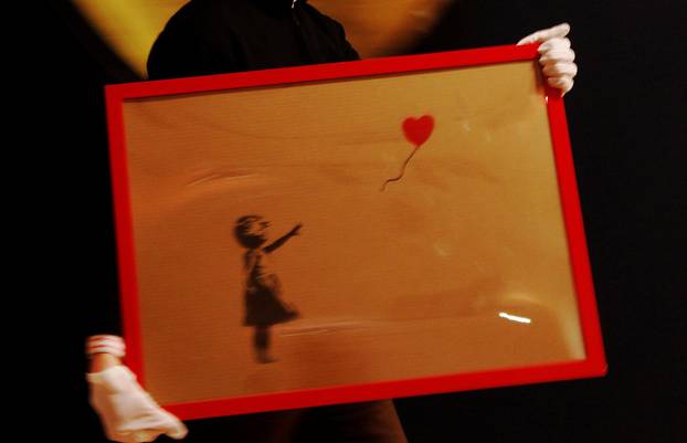 FILE PHOTO: An employee walks with artist Banksy's "Girl and Balloon" 2009 signed and inscribed For Mike, past artist  Ryan Callanan's (known as RYCA) "Mega Heart" 2011 at Bonhams auction house in London