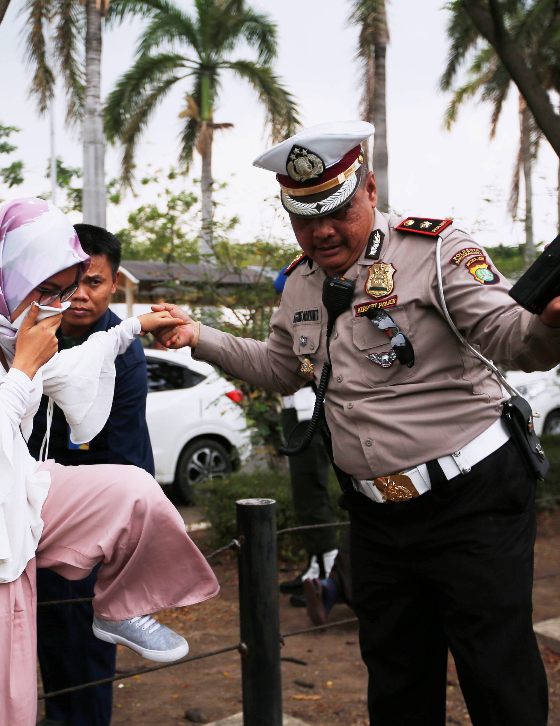 A policeman helps a woman who is a relative of a passenger of Lion Air flight JT610 that crashed into the sea, as she arrives at a crisis center at Soekarno Hatta International airport near Jakarta