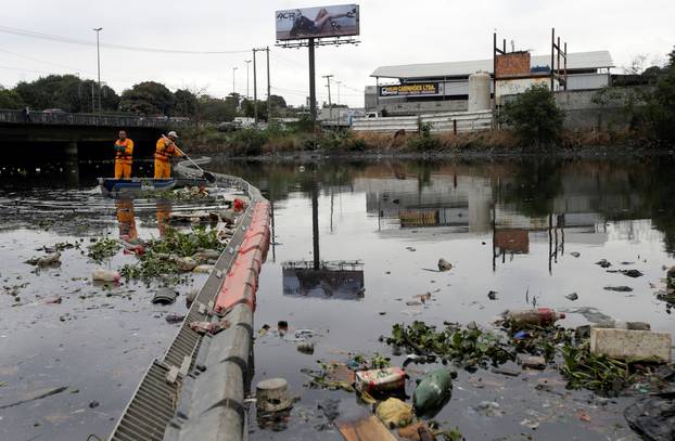 Men work cleaning up the garbage next to an ecobarrier at Meriti River which flows into Guanabara Bay, in Duque de Caxias, near Rio de Janeiro