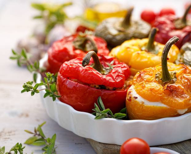 Roasted bell pepper with mushroom, rice, cheese and herbs filling in a baking dish on a white wooden table, close-up.