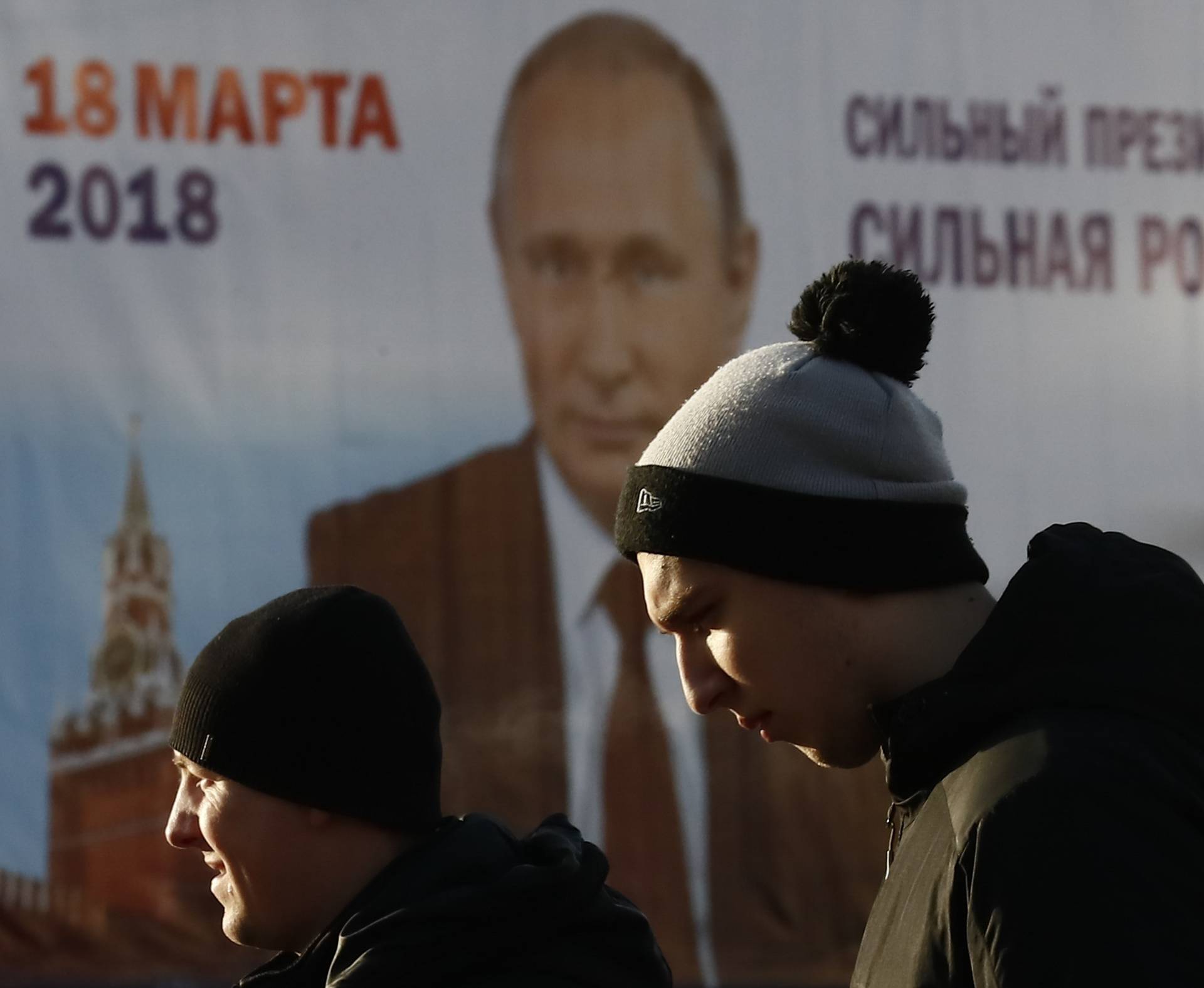 Men walk past a board, which advertises the campaign of Russian President Vladimir Putin ahead of the upcoming presidential election, in a street in Tula