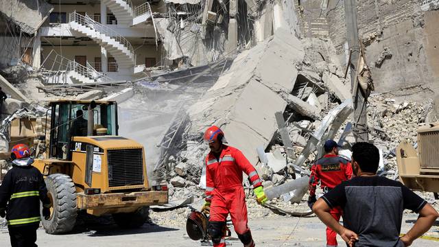 Firefighters remove debris to find bodies of people at the site of a collapsed building in Baghdad