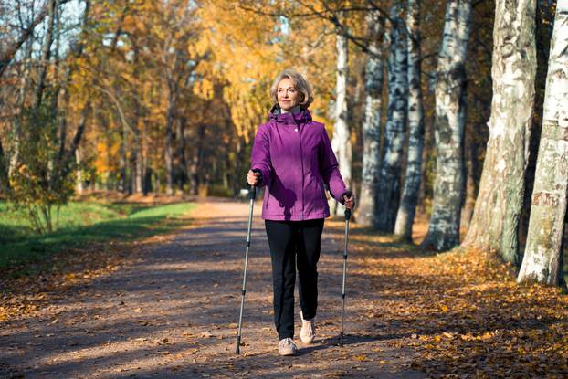 An,Elderly,Woman,Walks,Through,The,Park,On,Scandinavian,Sticks