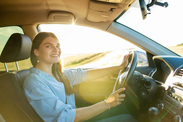 pretty woman singing while driving a car on road trip on summer day