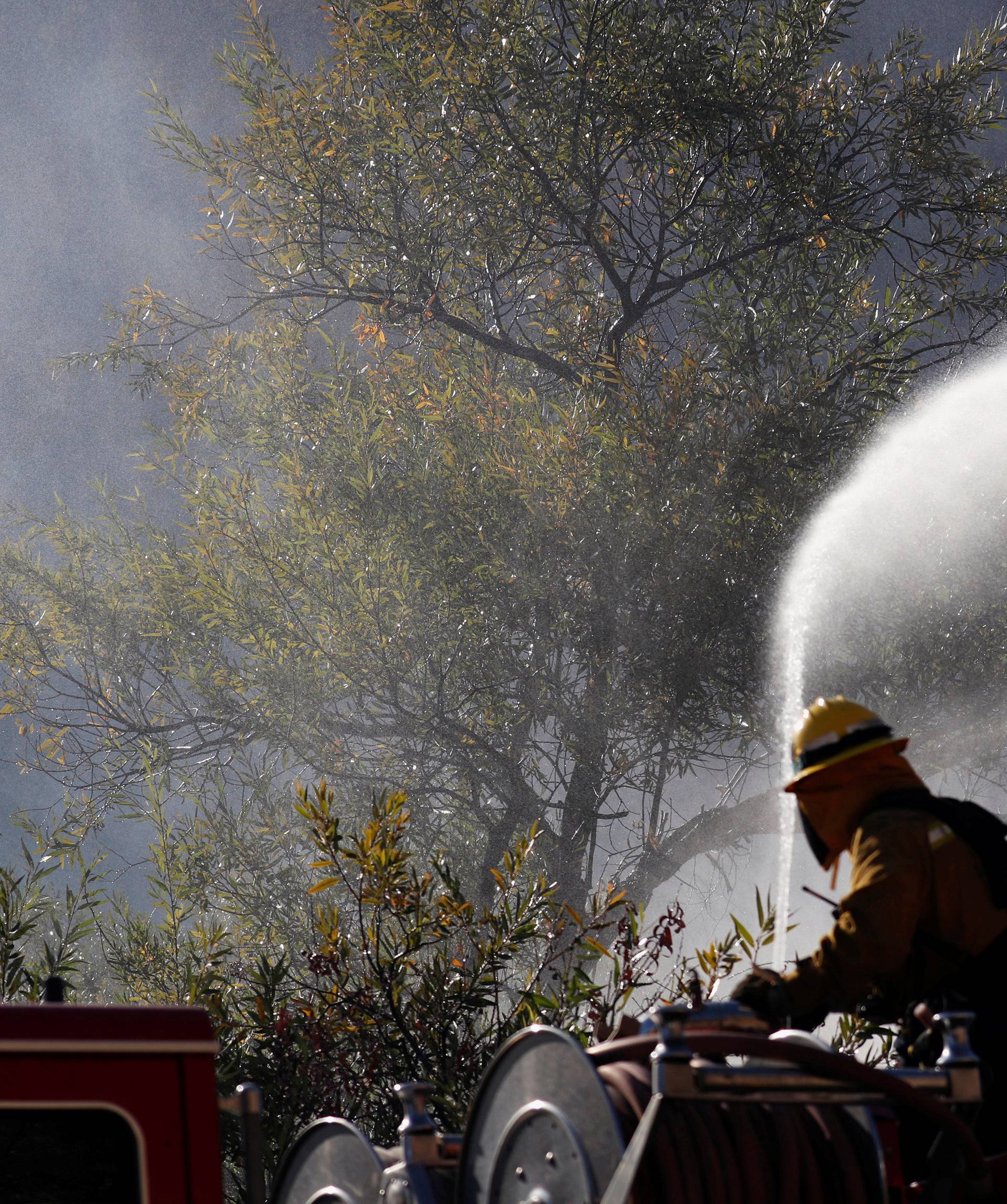 Firefighter sprays water from a hose while smoke is seen, as they battle the Woolsey fire in West Hills, Southern California