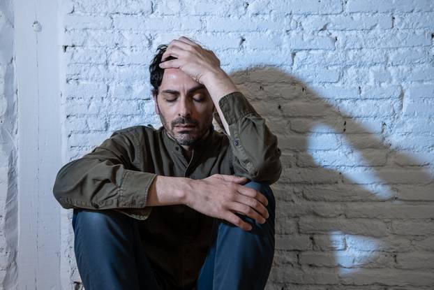 sad depressed man leaning against a wall in mental health concept