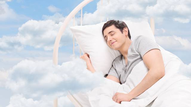 Joyful man sleeping on a bed in the clouds