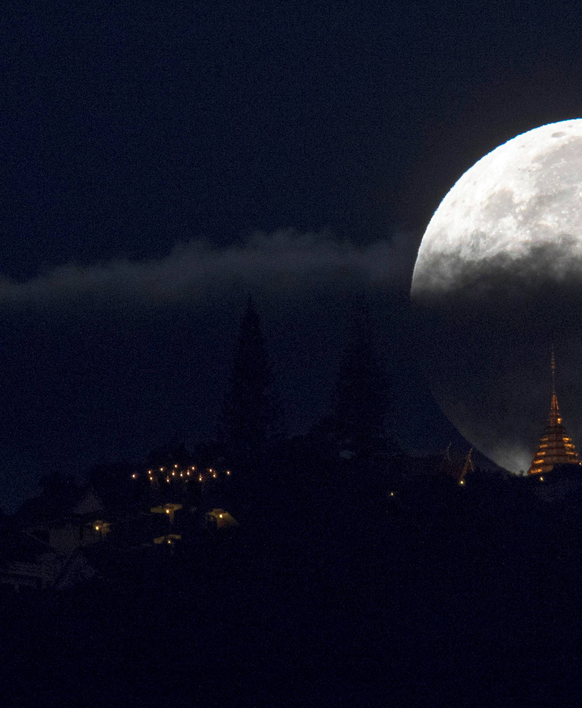 The supermoon is partly covered by clouds as it sets behind Wat Phrathat Doi Suthep in the northern capital of Chiang Mai