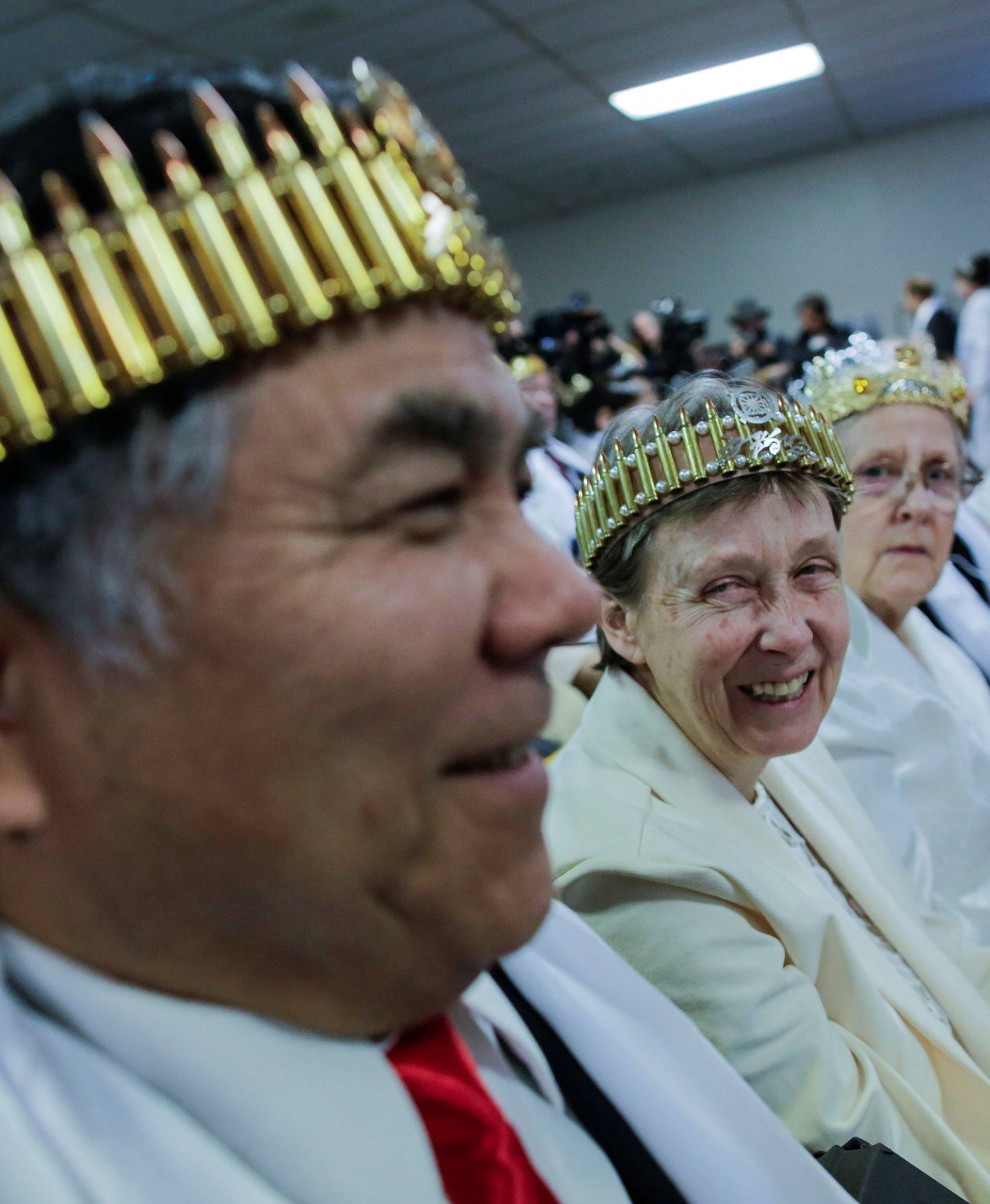 A couple wearing bullet crowns sit with their AR-15-style rifles in their cases, as people attend a blessing ceremony at the Sanctuary Church in Newfoundland