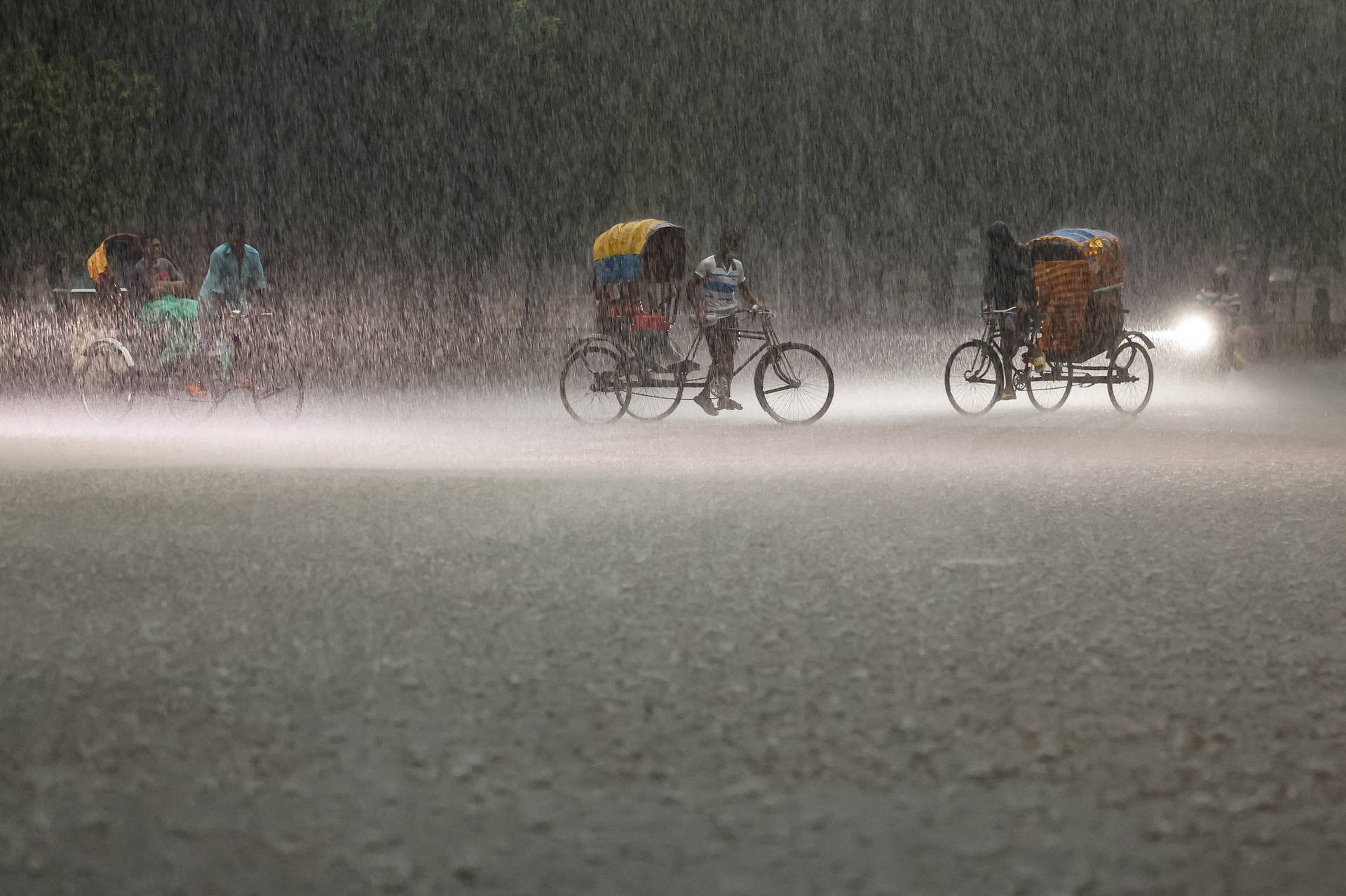 People riding on rickshaws during a downpour in Dhaka