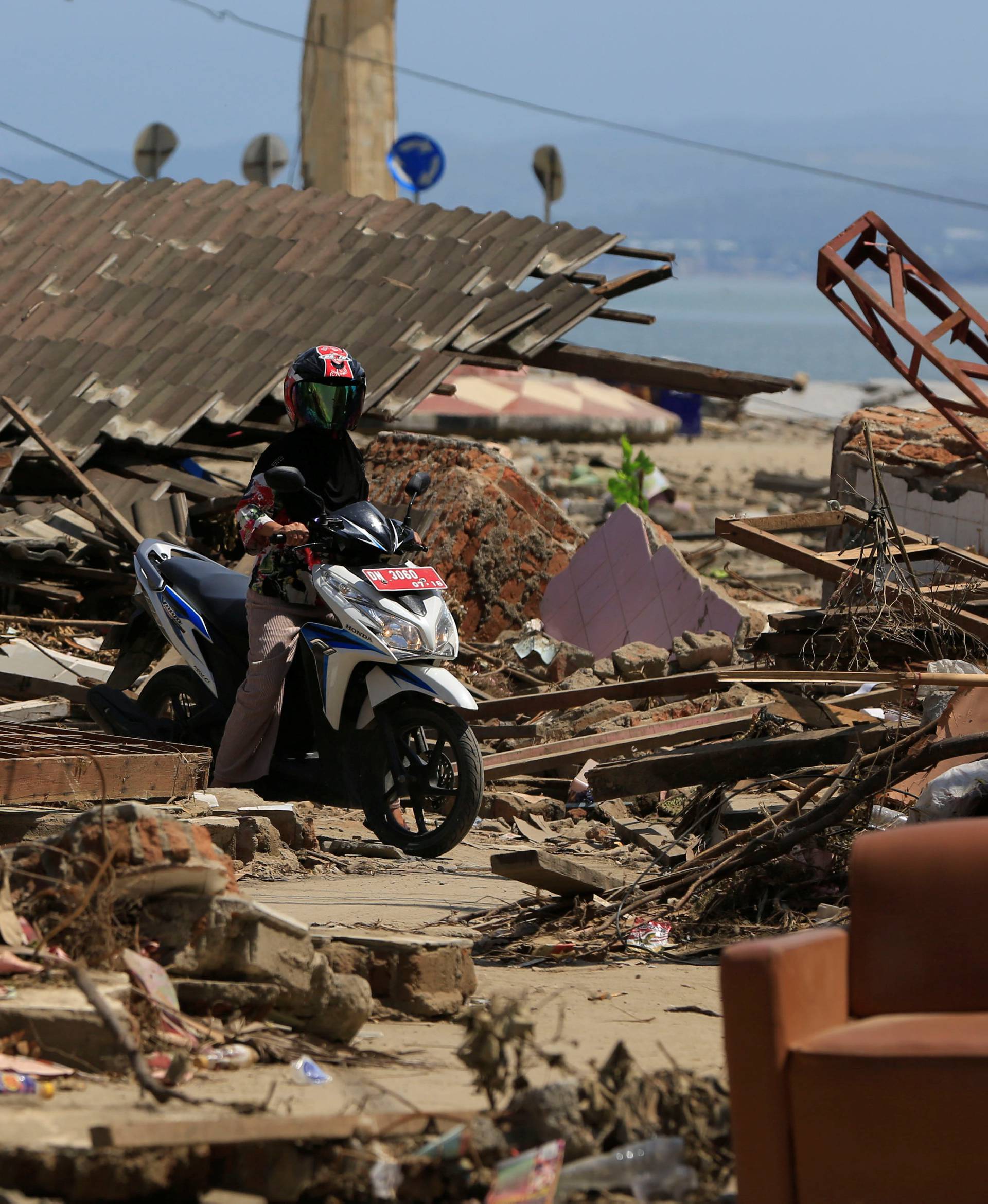 A resident rides her motorcycle among debris after the tsunami in Palu