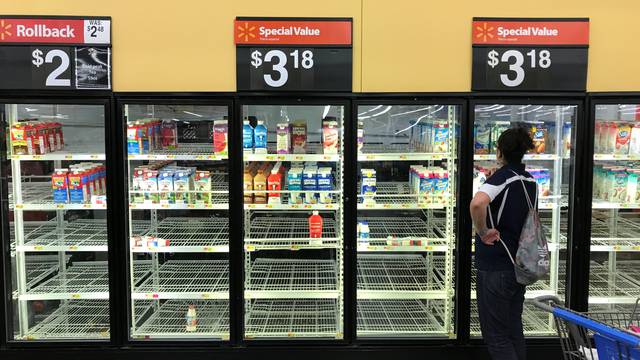 A unidentified woman looks over bare refrigerator shelves in a Walmart store in Houston
