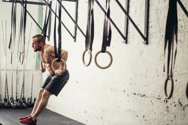 fit man pulling up on gymnastic rings.