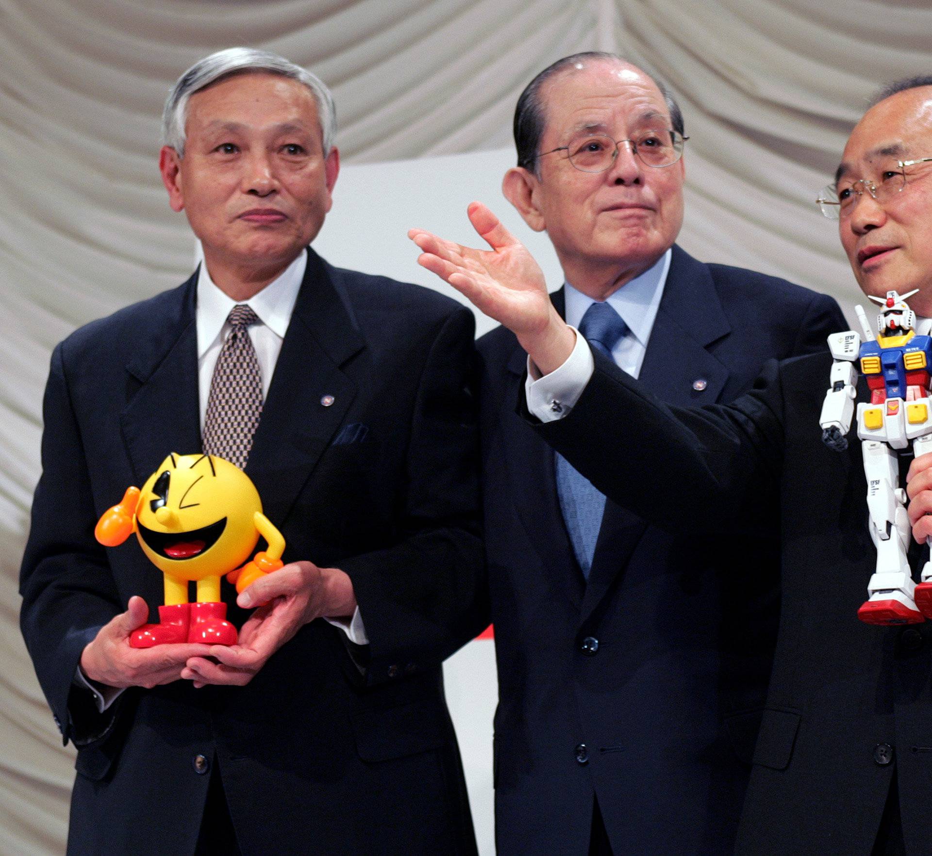 FILE PHOTO- Japanese toy maker Bandai Co President Takasu poses for photographers with Nakamura, chairman and founder of videogame company Namco Ltd, creator of "Pac-Man", and Vice-Chairman Takagi