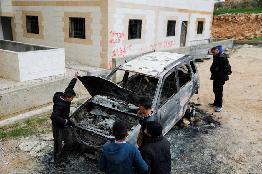 People check a damaged car, which Palestinians say was burned by Israeli settlers, near Hebron