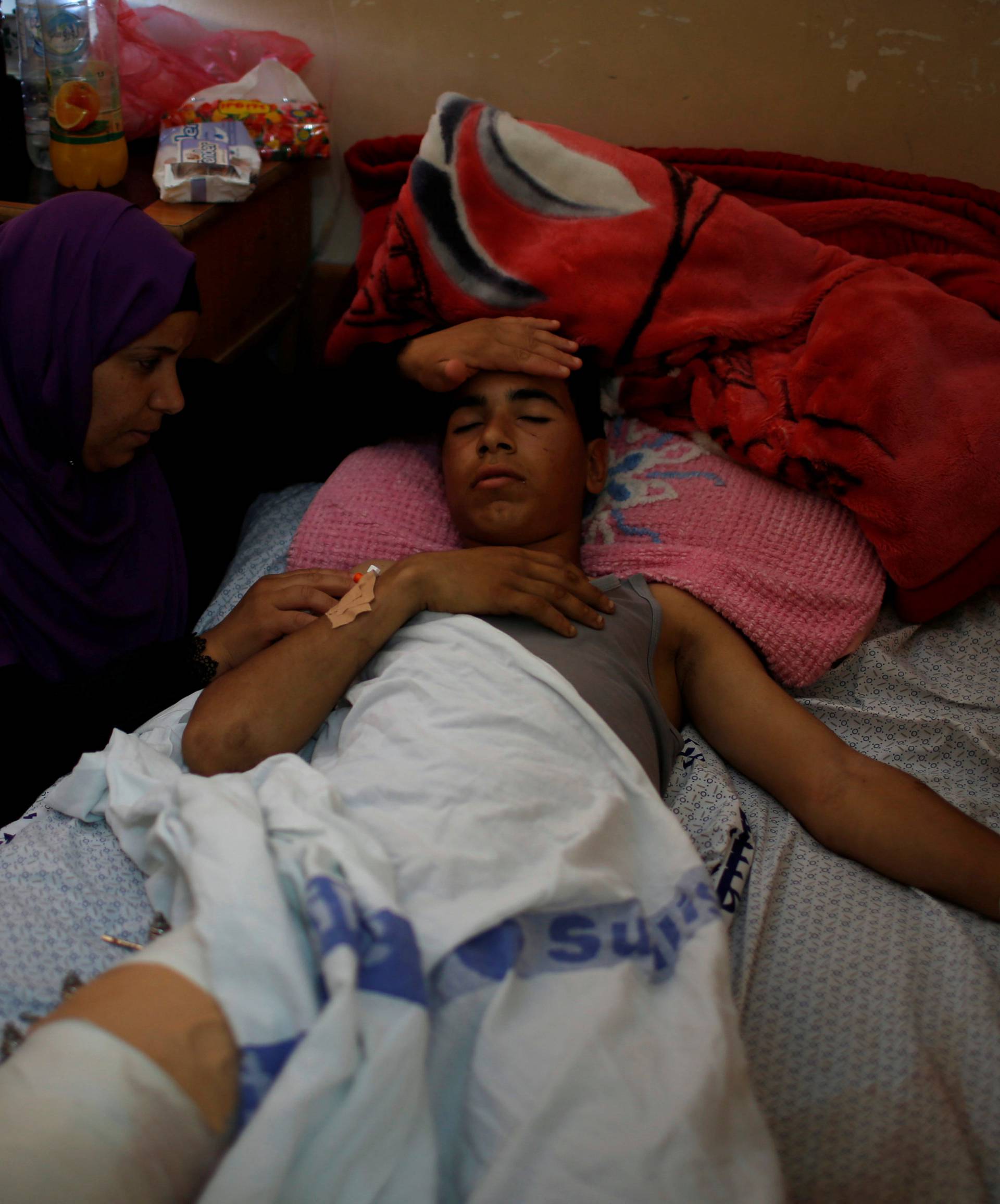 Mother of an injured Palestinian sits next to him as he lies on a bed at a hospital in Gaza City