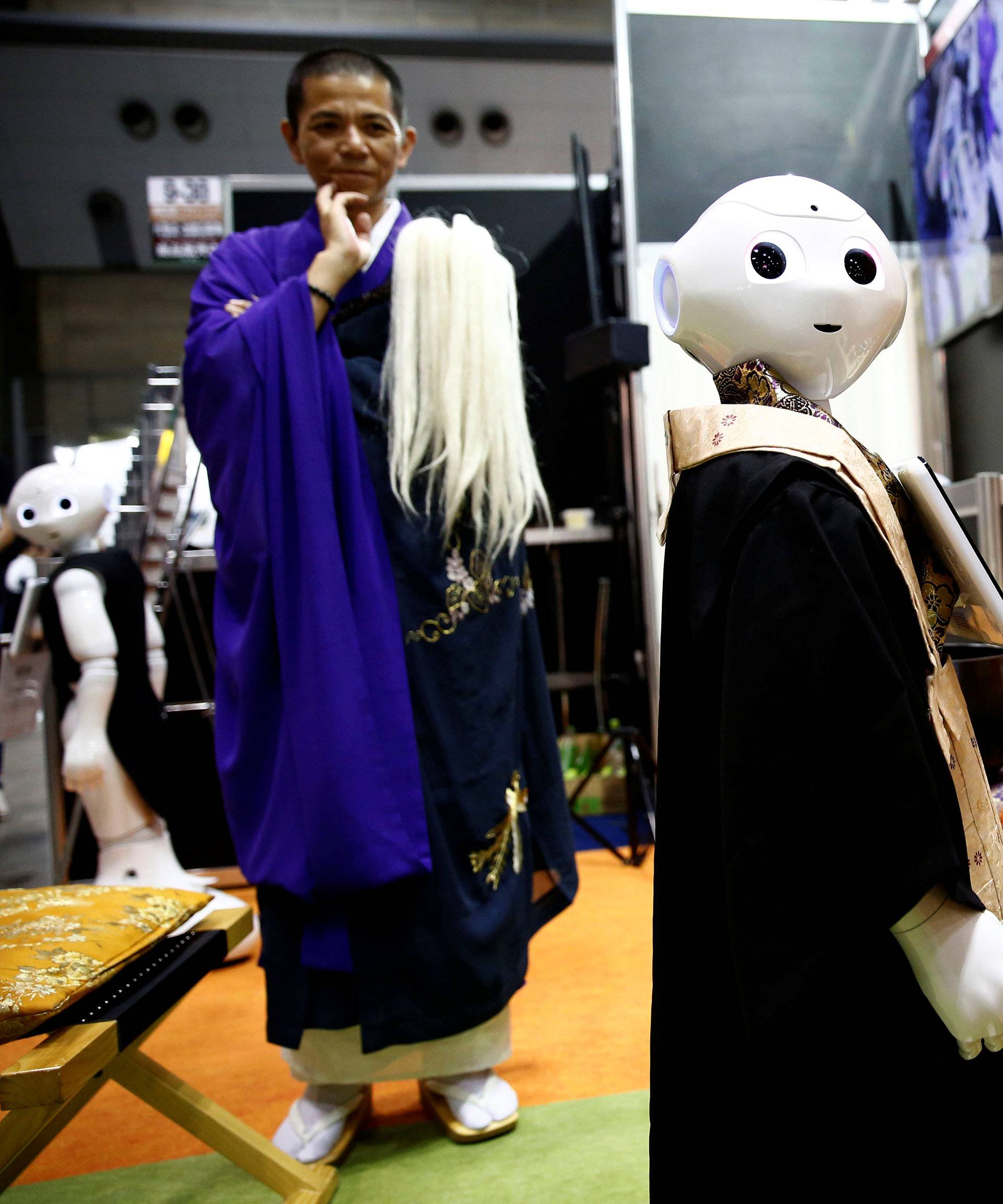 A Buddhist monk looks at a 'robot priest' wearing a Buddhist robe during its demonstration at Life Ending Industry EXPO 2017 in Tokyo