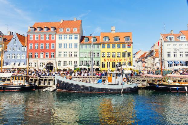 Copenhagen, Denmark - May 20, 2023: Scenic view famous colorful house building at Copenhagen Nyhavn harbour canal against blue sky on sunny day. Boats moored at european danish landmark sightseeing