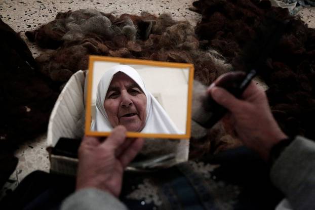 Ezzeya Daraghmeh, an 82-year-old Palestinian woman who said she has kept parts of her hair she cut over 67 years, looks at herself in a mirror as she stuffs a pillow with her hair, in the West Bank town of Tubas