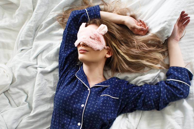 Cute blonde in her bed in blue pajamas and sleep mask, top view