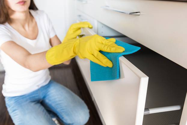 A young woman from a professional cleaning company cleans up at home. A man washes the kitchen in yellow gloves with cleaning supplies stuff.