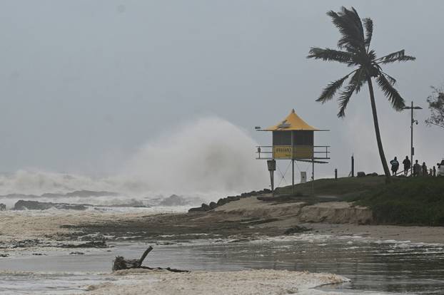 People stand as waves crash against the shore next to a lifeguard tower during winds caused by Cyclone Alfred, on the Gold Coast