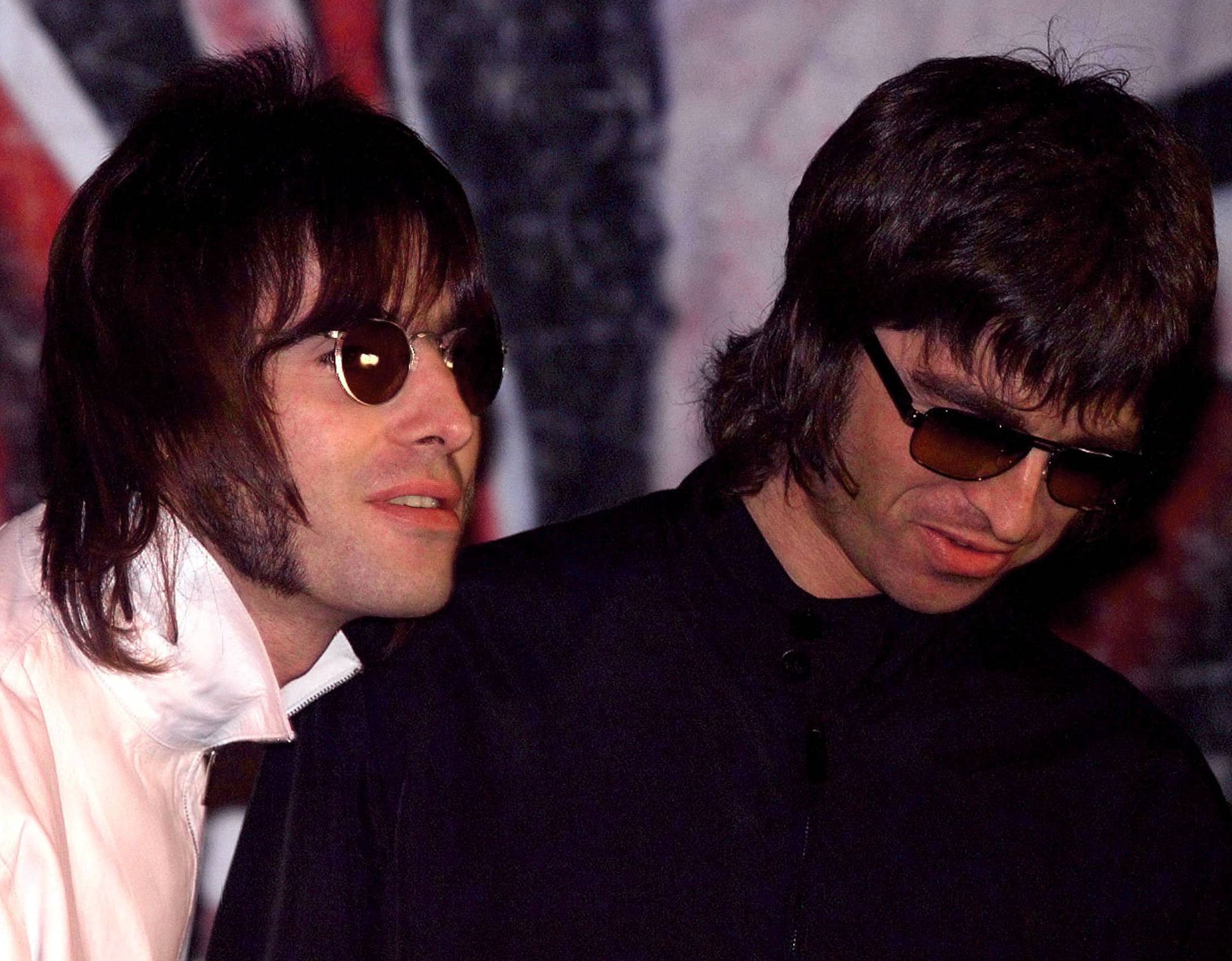 FILE PHOTO: Liam and Noel (R) Gallagher, of the British rock band Oasis, wait for the start of a news conference at a pub in London