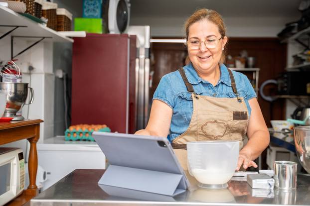 Smiling,Woman,Pastry,Chef,Checks,Recipe,On,Digital,Tablet,While