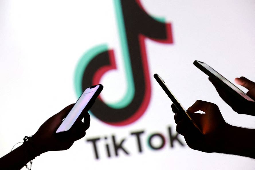 FILE PHOTO: Illustration shows teenagers pose for a photo while holding smartphones in front of a TikTok logo