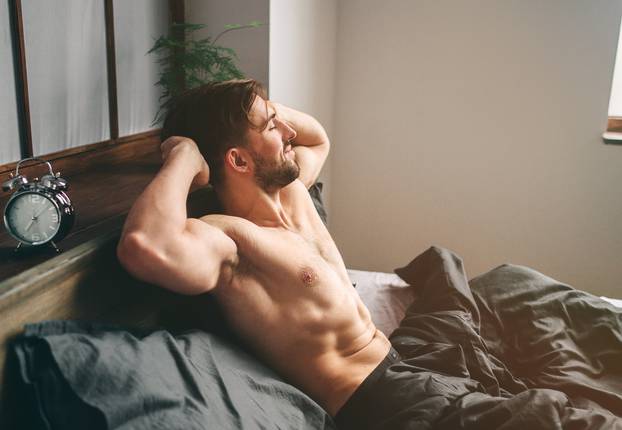 Carefree guy enjoying new day. Sexy, happy bearded man in bed