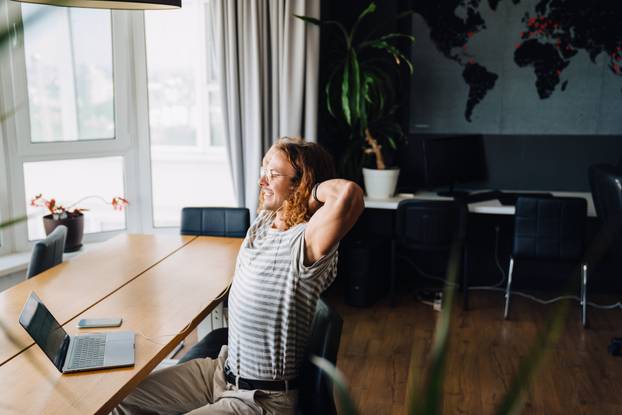 Young man using laptop and earphones while sitting by table in office