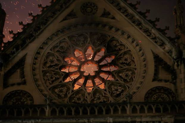 Sparks and flames are seen through a destroyed stained glass window as the Notre Dame Cathedral burns in Paris