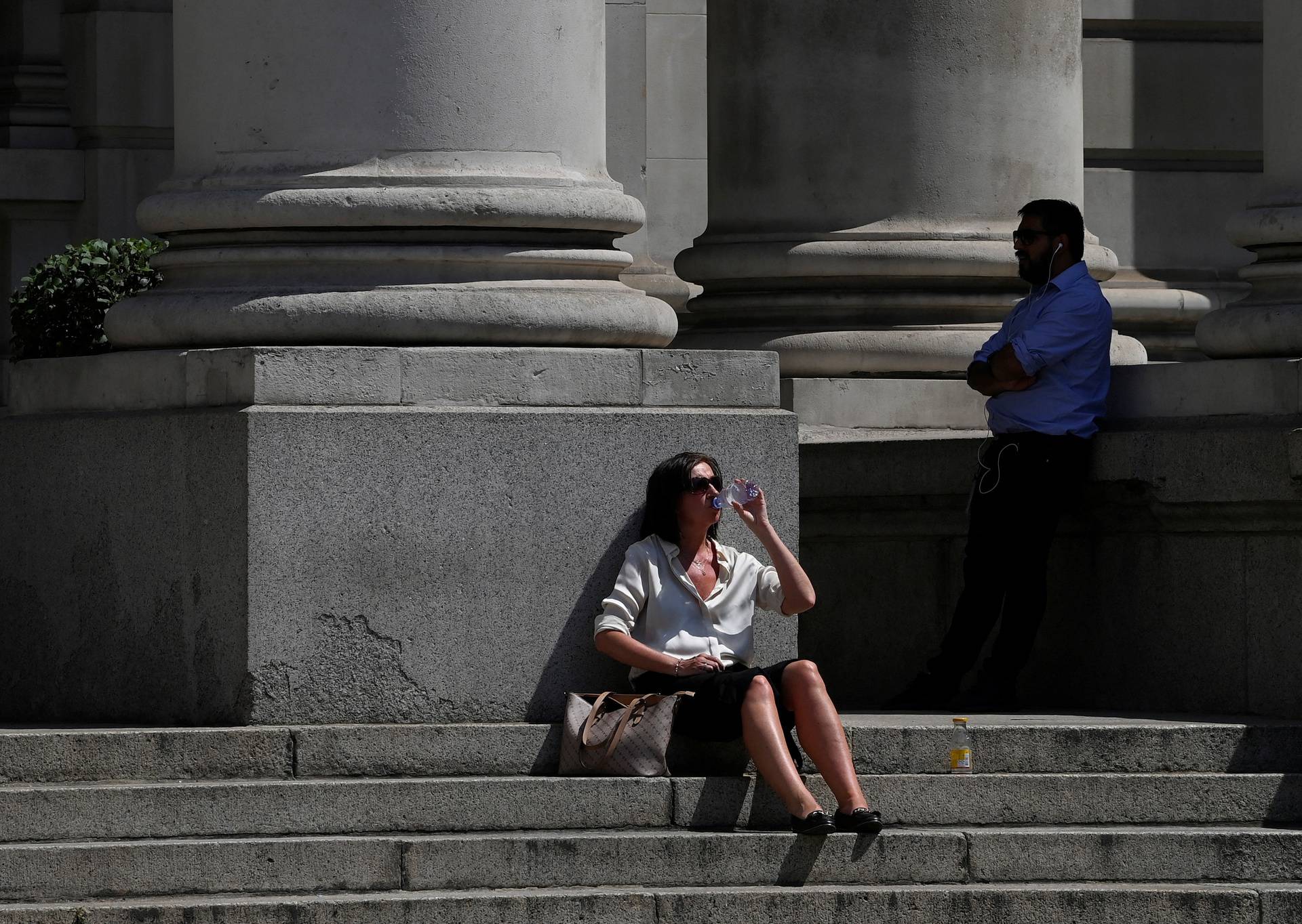 A drinks water during the hot weather in the City of London financial district, London