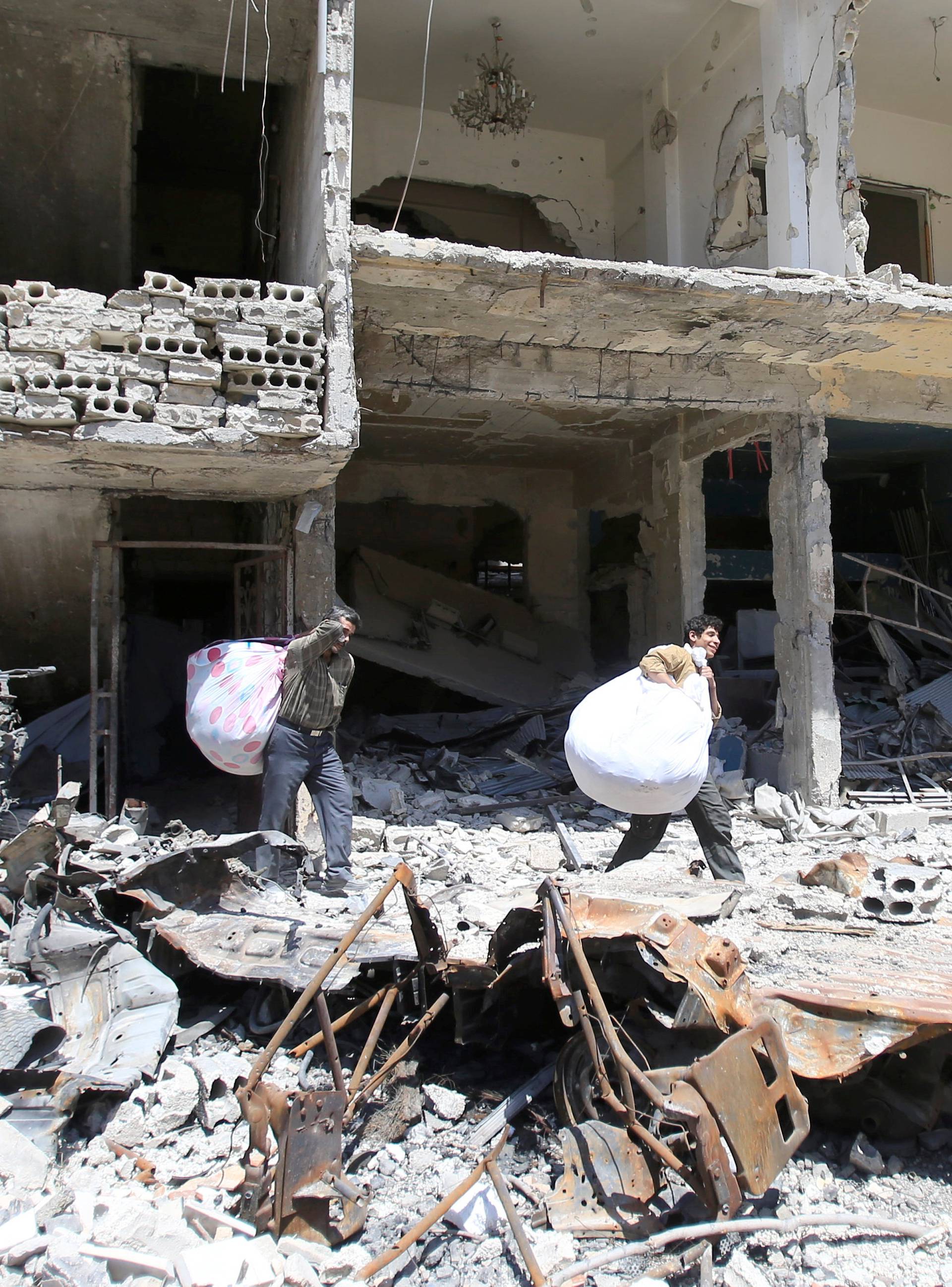 People hold belongings as they walk on the rubble of damaged buildings in the city of Douma, Damascus