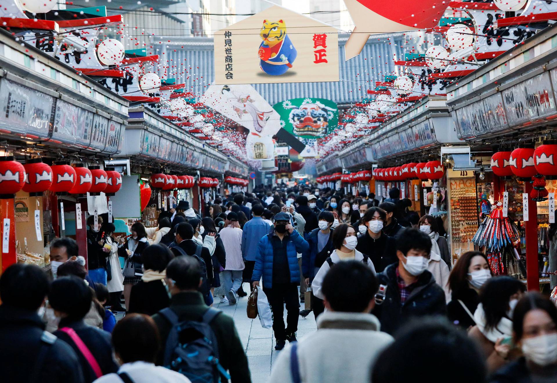 Visitors wearing protective face masks walk under decorations for the New Year at Nakamise street leading to Senso-ji temple at Asakusa district in Tokyo