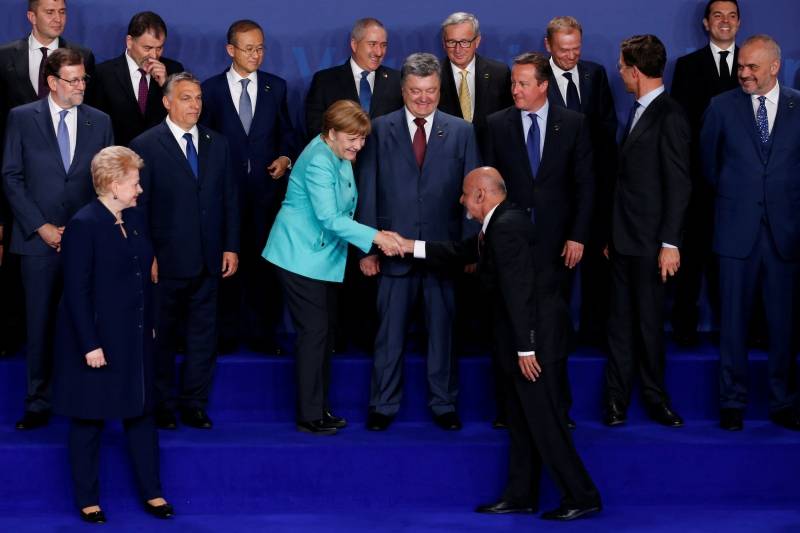 Merkel shakes hands with Ghani as they participate in a family photo at the NATO Summit in Warsaw, Poland