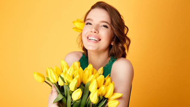 portrait of cheerful woman with bouquet of yellow tulips isolated on orange