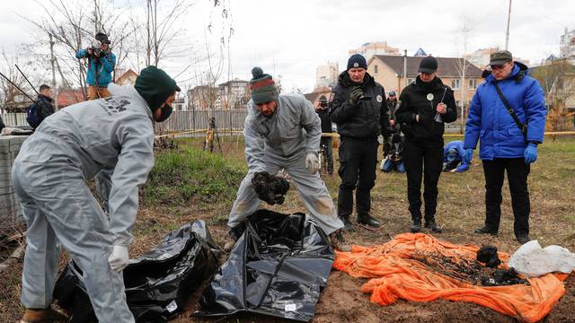 Ukrainian forensics investigators place remains of burned civilians exhumed from a grave in body bags, in the town of Bucha