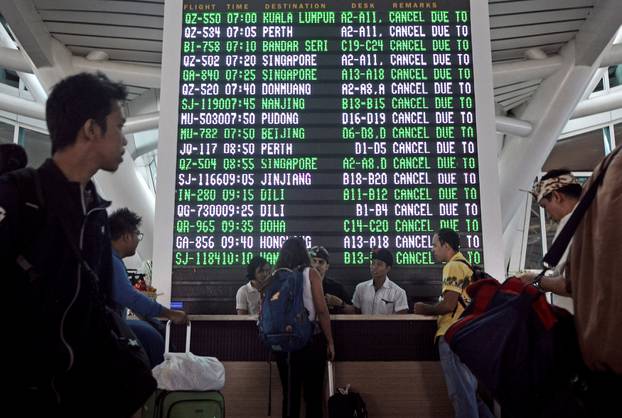 Passengers ask staff about their flights near the flight screen after Ngurah Rai airport closed their operation due to eruption of Mount Agung in Bali resort island